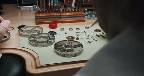 Un horloger place soigneusement les petites pièces d'une montre-bracelet dans un récipient métallique pour le nettoyer