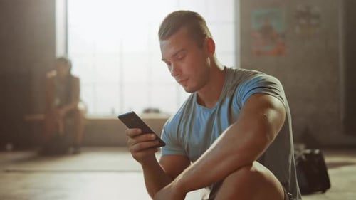 Handsome and Masculine Athletic Young Man is Using a Smartphone while Sitting on a Floor in a Loft