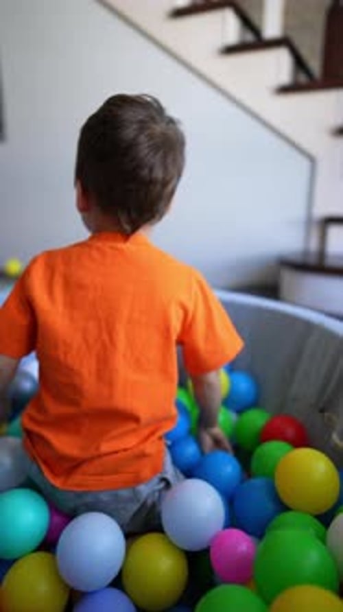 Energetic baby boy tumbling in the colorful balls in the dry pool.