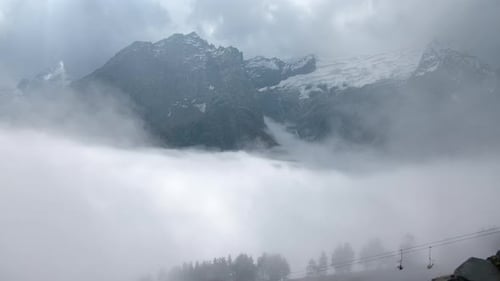 Mountain landscape of lifts in clouds and snowy peaks
