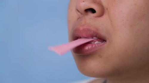 Young woman chewing gum and blowing bubble gum on blue background.