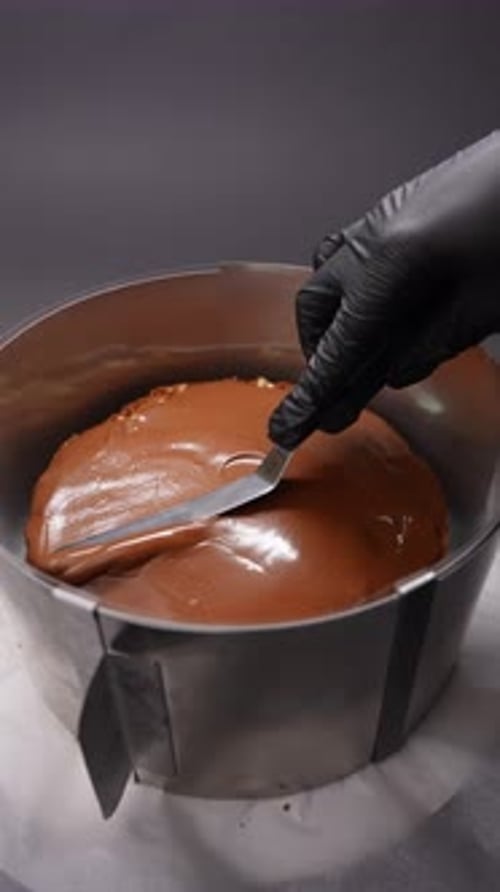 Brown Chocolate Cake being Frosted by Gloved Hand