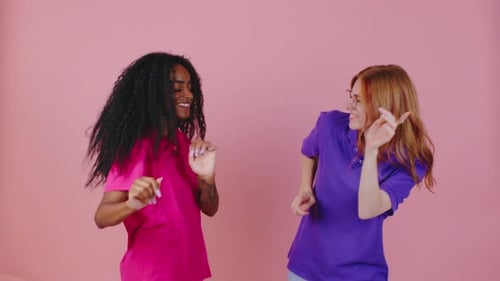Two Smiling Women Dancing In Front of Pink Backdrop
