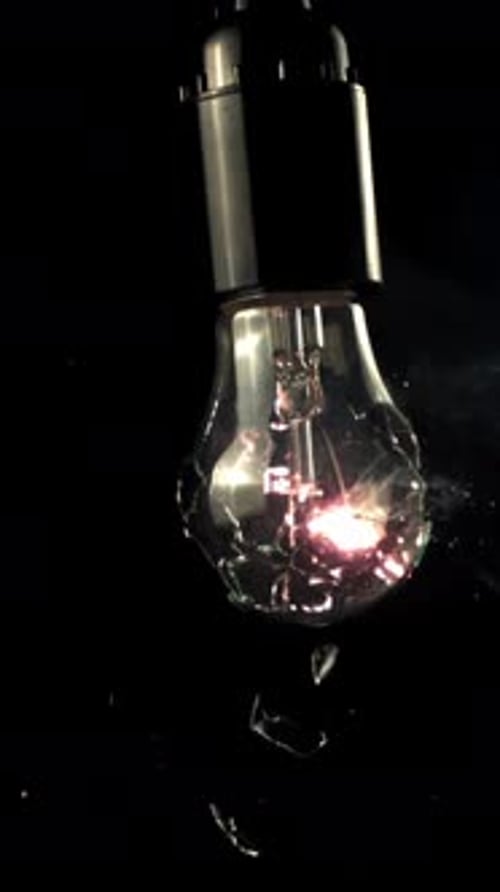 Super-Slow-Motion-Glühbirne zerbricht in Rasseln auf schwarzem Hintergrund