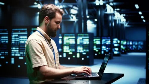 Man Typing on Laptop in Dark Server Room