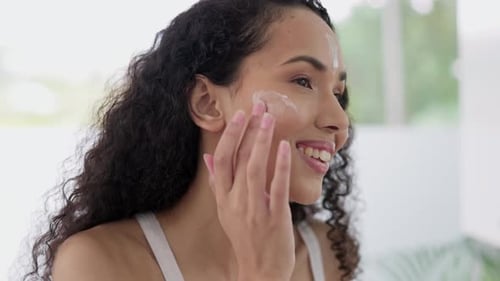Young Woman Applies Lotion to Face in Bathroom