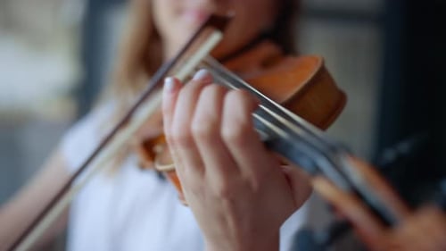 Closeup of young woman's hands gracefully playing violin in living room at home
