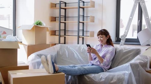 Moving, People And Real Estate Concept - Happy Smiling Asian Woman With Smartphone And Boxes At N...