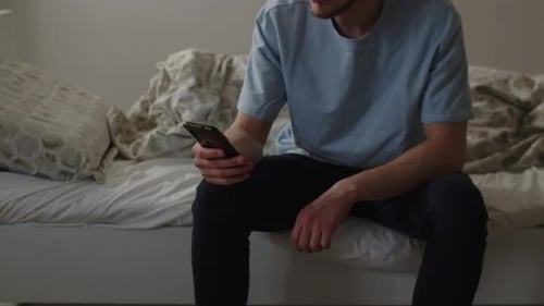 Cropped View of a Man Sitting on the Bed and Scrolling on the Smartphone Screen A Newly Woken Man