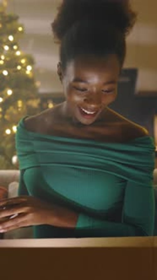 Excited woman opens gift near Christmas tree indoors