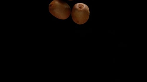 Bunch of kiwi fruit falling down isolated on black background, super slow motion view
