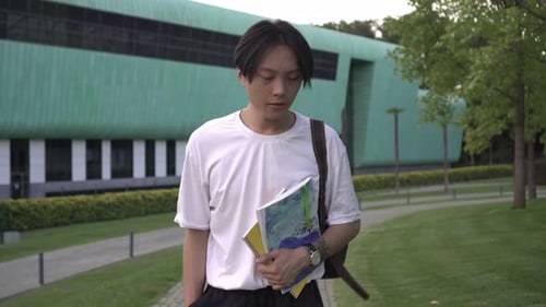 A Young Asian Male Student Walks Against the Backdrop of a University or College