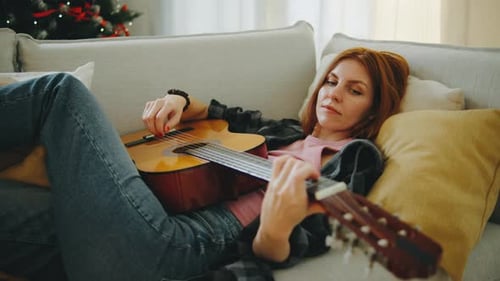 Woman Lying on Couch Playing Acoustic Guitar Indoors
