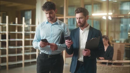 Two Men with Phones Walking Forward in Office