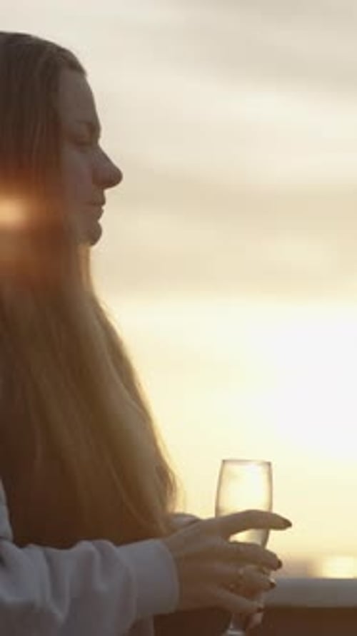 Vidéo verticale. Vidéo verticale. Une femme sur le balcon boit du champagne, Bright Sunbeams Play
.