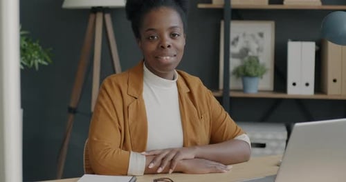 Slow Motion Portrait of Successful African American Lady Sitting at Desk in Office Smiling