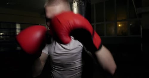 Professional Boxer Trains in the Night Gym Looks Seriously at the Camera and Boxing in Boxing Gloves