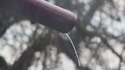 Une pluie légère tombe par la fenêtre et un jet d'eau s'écoule de la gouttière vers le sol