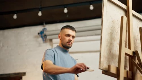 In einem Kunstworkshop macht ein Künstler in einem blauen T-Shirt breite Striche auf der Leinwand mit breit und flach