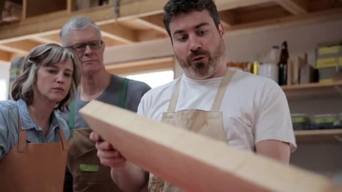 Carpenter Explaining Wood Plank to Coworkers in Workshop 3539 Years