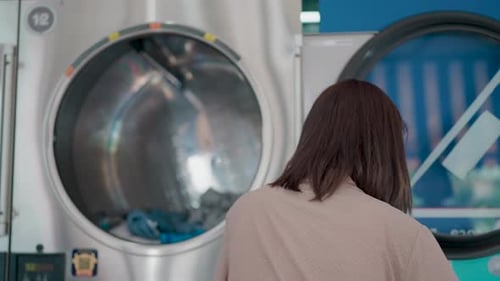 Woman Loading Clothes Into Commercial Washing Machine