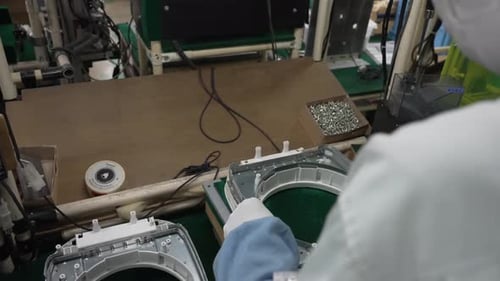 Un ouvrier de la chaîne de montage installe des vis dans le boîtier intérieur du cuiseur à riz IH avec alimentation électrique
