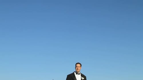 Groom in Tuxedo Barefoot Leaping High Against Blue Sky