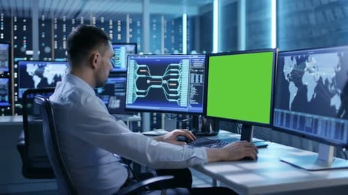 Controlador técnico/operador que trabaja en su estación de trabajo con varias pantallas (pantalla verde simulada)