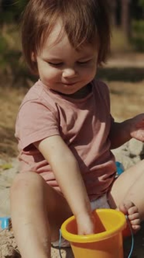 Vidéo verticale Un jeune enfant joue énergiquement à l'extérieur avec un seau jaune vif dans la nature