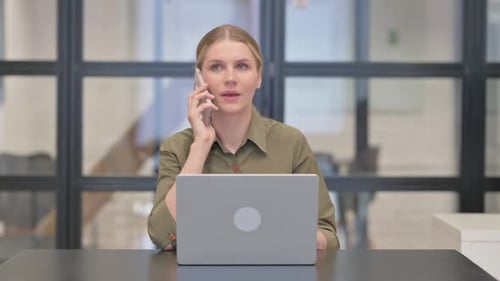 Woman Talking on Cell Phone at Desk with Laptop