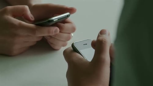 Closeup of Hands Using Two Mobile Phones