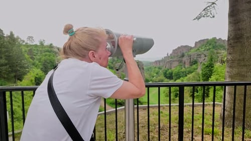 Female looks through observation telescope at scenic lookout point