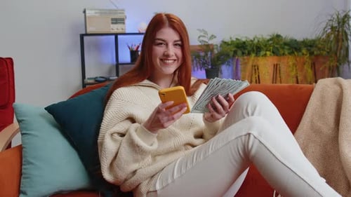 Woman with Cash Using Phone on Couch at Home