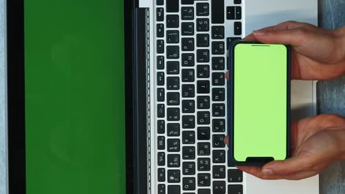 Woman sitting at office desk and watching on smartphone with green screen