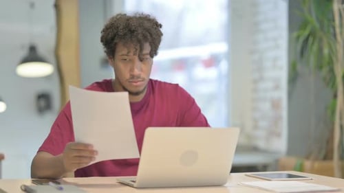 Young Adult Working on Laptop with Documents at Desk