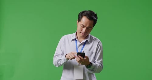 Asian Business Man Using Mobile Phone While Walking On Green Screen Background In The Studio