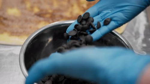 Gloved Hands Mixing Chocolate Chips in Steel Bowl