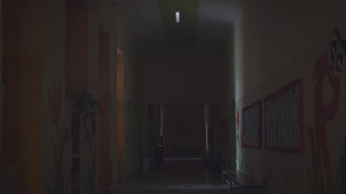 An empty school hallway in the dark suddenly illuminates from the switched-on fluorescent lamps and
