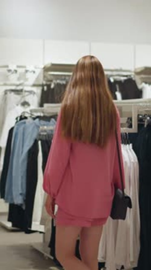 Lady in Pink Dress Browsing Clothes in a WellLit Store