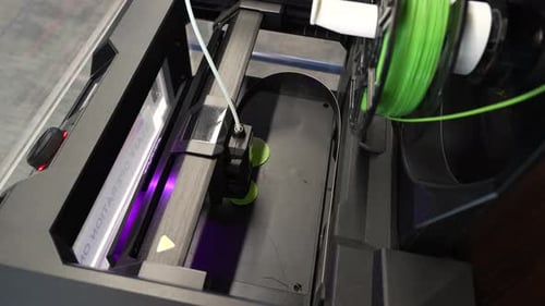 Top view shot shows the printer head and feed wire of a 3D printer at work.