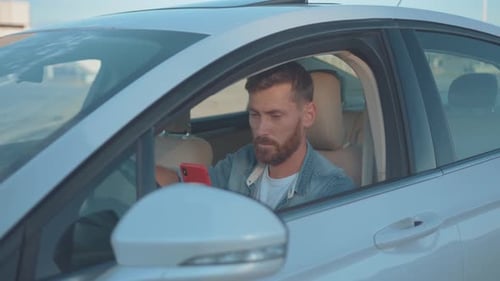 Man Looks at Smartphone in Car with Concern