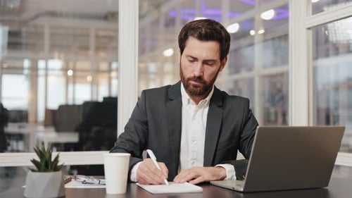 Businessman Working on Laptop and Taking Notes in Office