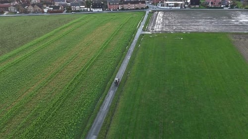 Tractor on path on agricultural farm fields in winter. Rainy day in american suburb. Top down shot.