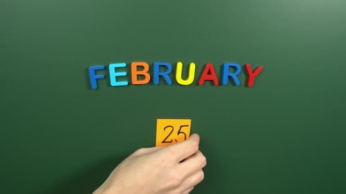 Hand sticking a sticker 25 February calendar day on school board. 25 date of February. Twenty five