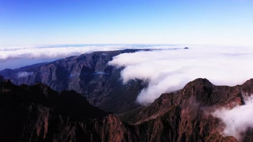 Aerial view overlooking mountain peaks and clouds, in Madeira - pan, drone shot