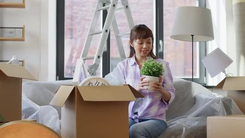 Happy asian woman unpacking boxes in new home real estate slow motion
