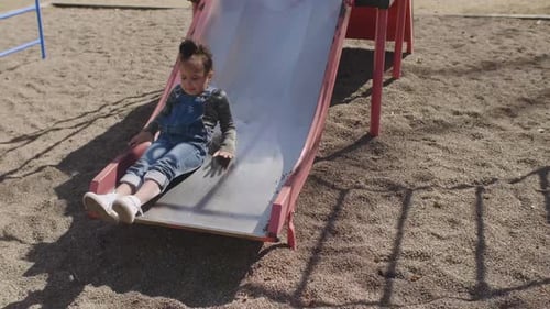Toddler girl enjoying a sunny day sliding down a playground slide in suburban Canada