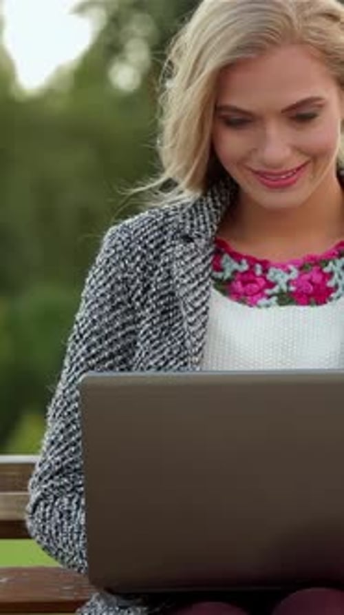 Joyful Girl Student Smiles While Using Her Laptop on a Sunny Park Bench