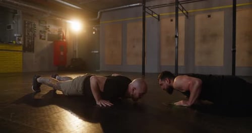 Men Doing Pushups Together in Dark Gym