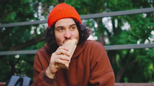 The Man Sits Quietly on a Park Bleacher Enjoying His Hot Dog in the Fresh Air He Seems to Appreciate